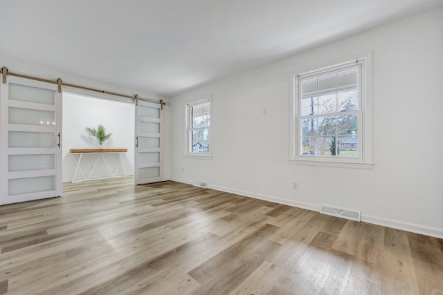 spare room featuring visible vents, baseboards, a barn door, and wood finished floors