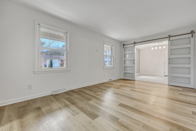 unfurnished bedroom featuring a barn door, baseboards, visible vents, and light wood finished floors