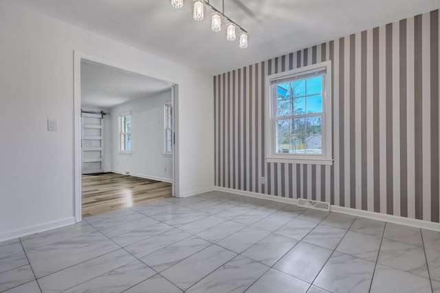 empty room featuring baseboards, wallpapered walls, and a barn door