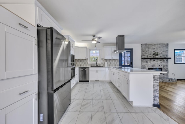 kitchen with backsplash, a peninsula, island range hood, marble finish floor, and stainless steel appliances