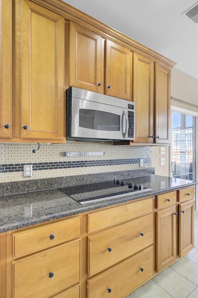 kitchen with light tile patterned floors, backsplash, black electric stovetop, and dark stone counters