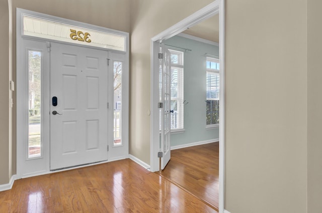 entryway with light wood-type flooring, crown molding, and a wealth of natural light