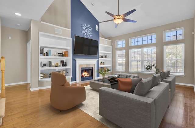 living room featuring built in shelves, ceiling fan, high vaulted ceiling, wood-type flooring, and a tiled fireplace