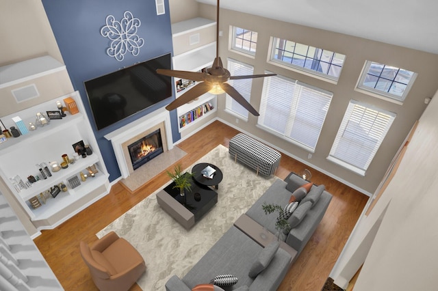 living room with hardwood / wood-style flooring, ceiling fan, a towering ceiling, and a fireplace