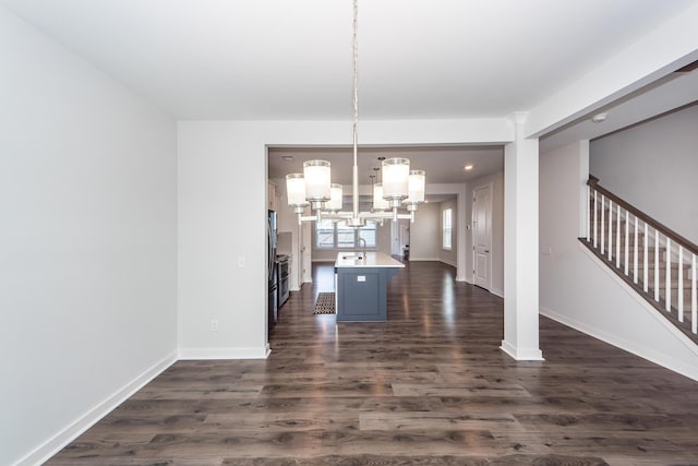 unfurnished dining area featuring stairs, baseboards, a notable chandelier, and dark wood finished floors