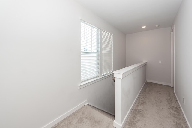 hallway featuring light carpet, an upstairs landing, and baseboards