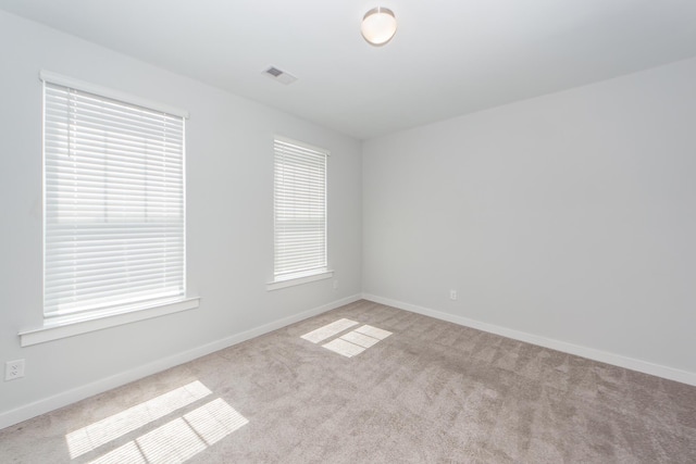 spare room featuring light colored carpet, baseboards, and visible vents
