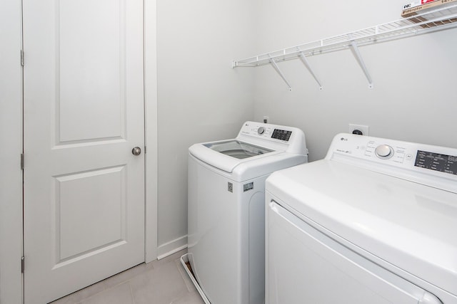 clothes washing area with light tile patterned floors, washer and dryer, and laundry area