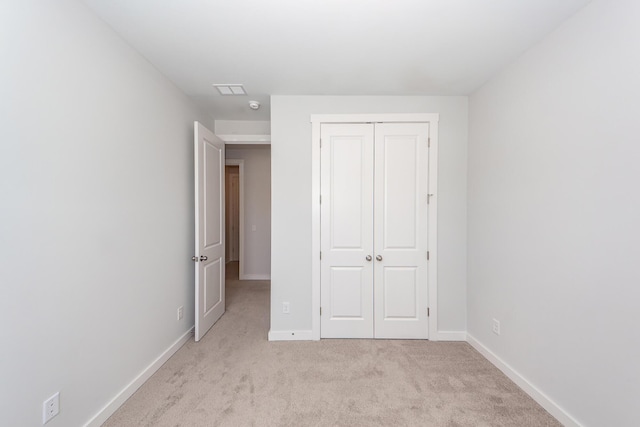 unfurnished bedroom featuring a closet, baseboards, light carpet, and visible vents