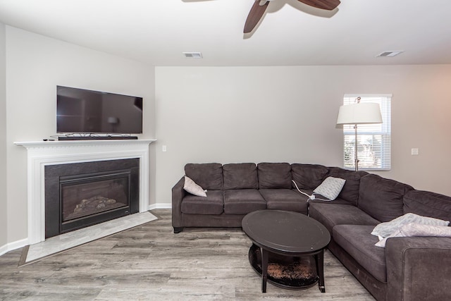 living area with a fireplace with flush hearth, ceiling fan, wood finished floors, and visible vents