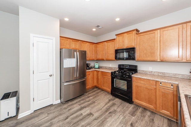 kitchen with light wood-style floors, light countertops, visible vents, and black appliances