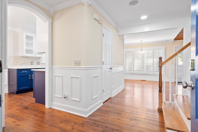 corridor with a wainscoted wall, stairway, crown molding, and wood-type flooring