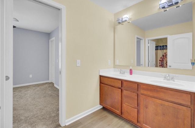 full bathroom featuring a sink, baseboards, wood finished floors, and double vanity