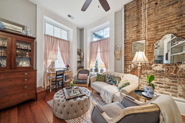 living area featuring dark wood-type flooring, ceiling fan, and brick wall