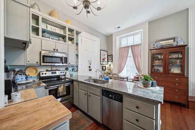 kitchen featuring dark wood-type flooring, sink, gray cabinetry, appliances with stainless steel finishes, and dark stone counters