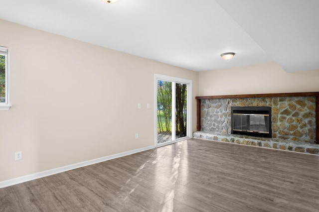 unfurnished living room featuring hardwood / wood-style flooring and a stone fireplace