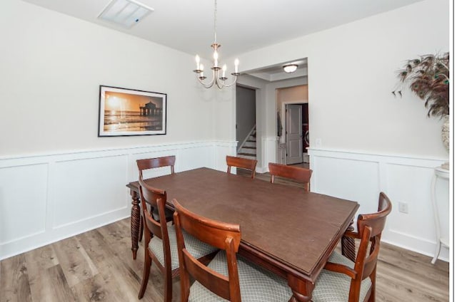 dining area with light wood-style floors, stairs, and a wainscoted wall