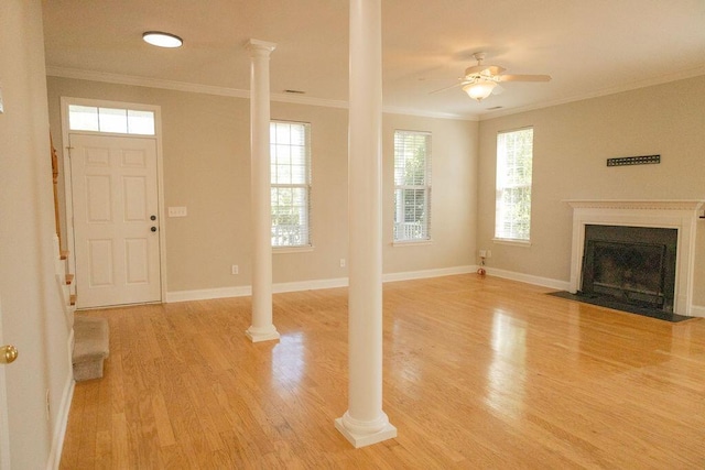 unfurnished living room with light wood-style flooring, a ceiling fan, a fireplace with flush hearth, ornate columns, and ornamental molding