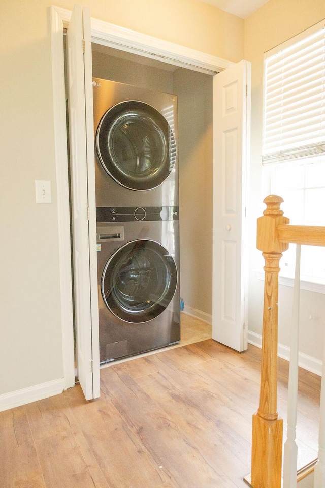 clothes washing area featuring baseboards, laundry area, stacked washer and dryer, and wood finished floors