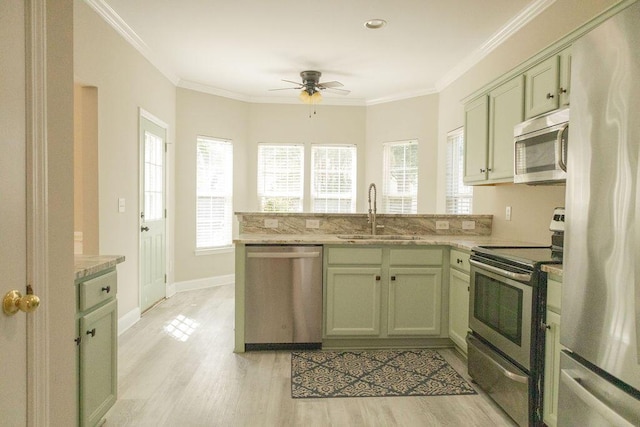 kitchen with a sink, stainless steel appliances, a ceiling fan, a peninsula, and green cabinets