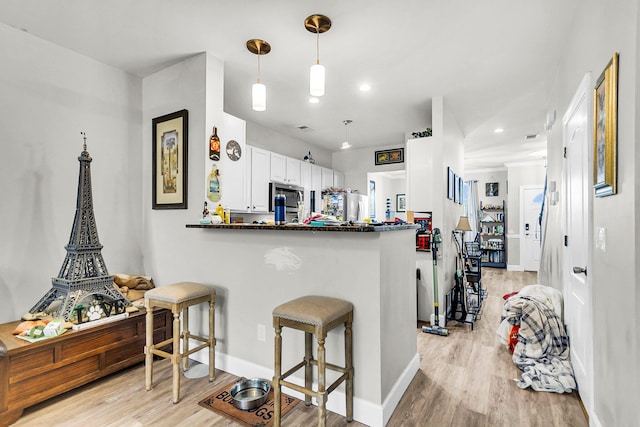 kitchen with hanging light fixtures, kitchen peninsula, light wood-type flooring, and white cabinetry