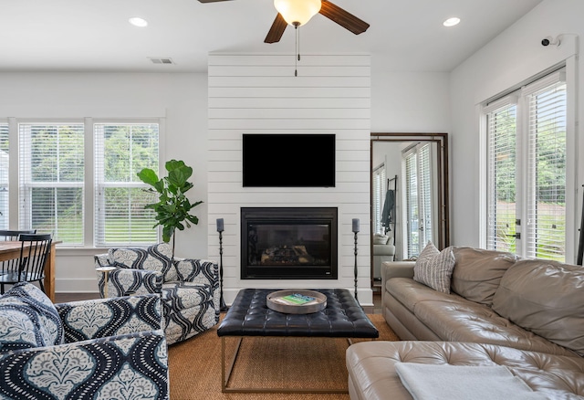 living room featuring a large fireplace, ceiling fan, hardwood / wood-style flooring, and plenty of natural light