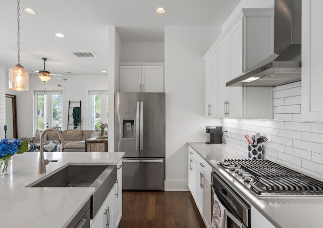 kitchen featuring dark hardwood / wood-style floors, wall chimney exhaust hood, appliances with stainless steel finishes, white cabinetry, and ceiling fan