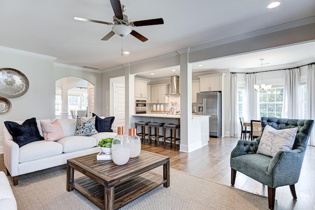 living room featuring light hardwood / wood-style flooring, ceiling fan with notable chandelier, and ornamental molding