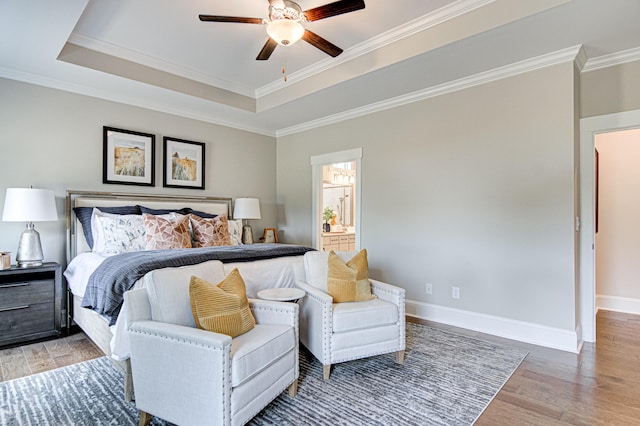 bedroom with a tray ceiling, ensuite bathroom, hardwood / wood-style floors, and ceiling fan