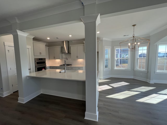 kitchen with crown molding, white cabinets, wall chimney range hood, and a notable chandelier