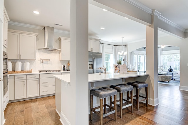 kitchen with light hardwood / wood-style flooring, wall chimney exhaust hood, an island with sink, a kitchen bar, and stainless steel appliances