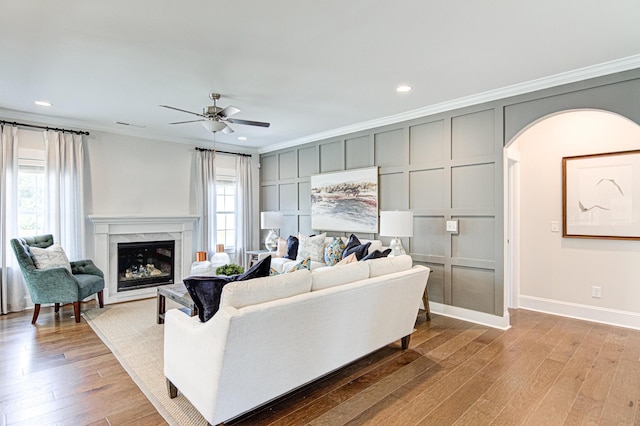 living room with ceiling fan, a premium fireplace, ornamental molding, and light hardwood / wood-style flooring