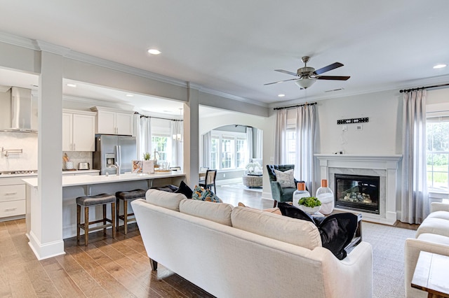 living room featuring a high end fireplace, light wood-type flooring, ceiling fan, and crown molding