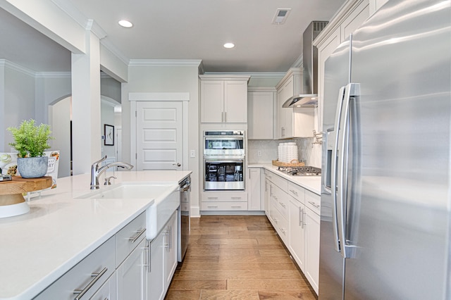 kitchen featuring appliances with stainless steel finishes, backsplash, light wood-type flooring, wall chimney exhaust hood, and white cabinets