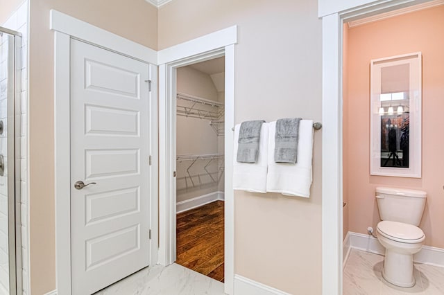 bathroom with toilet, a shower with shower door, and ornamental molding