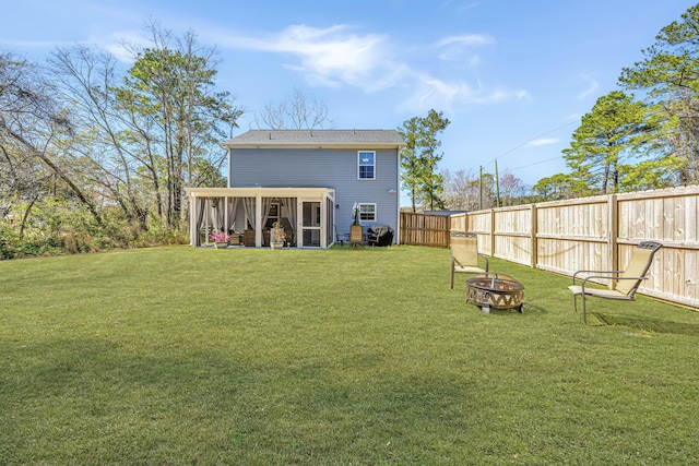 rear view of house featuring fence, a fire pit, a lawn, and a sunroom