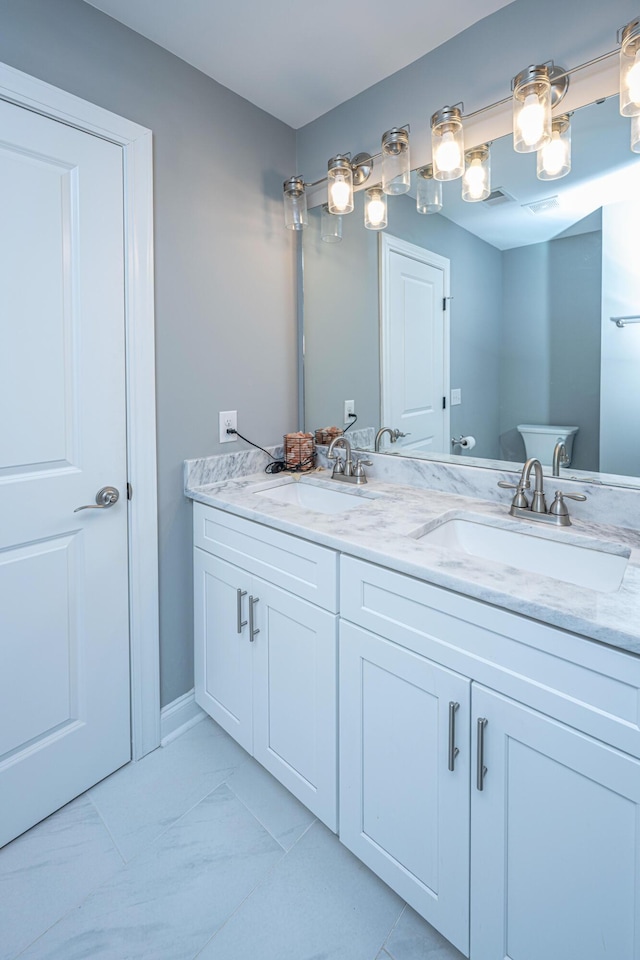 bathroom with double vanity, marble finish floor, toilet, and a sink