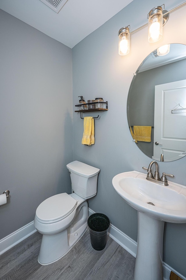 half bath featuring visible vents, toilet, a sink, wood finished floors, and baseboards