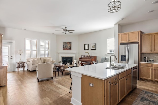 kitchen featuring a center island with sink, appliances with stainless steel finishes, light wood-type flooring, ceiling fan with notable chandelier, and sink