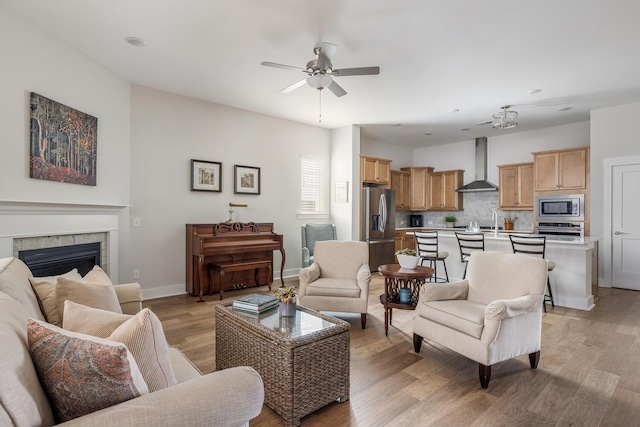 living room with ceiling fan, a tiled fireplace, and light hardwood / wood-style flooring