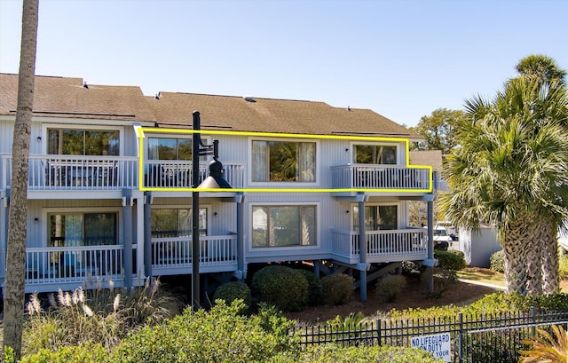 back of property featuring a balcony, a shingled roof, and fence