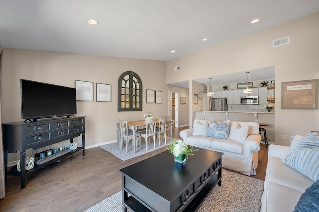 living area with recessed lighting, wood finished floors, visible vents, baseboards, and vaulted ceiling