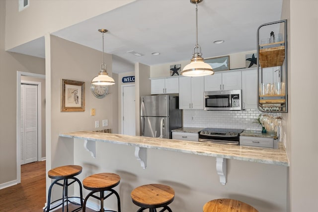 kitchen featuring a peninsula, white cabinetry, appliances with stainless steel finishes, light stone countertops, and tasteful backsplash