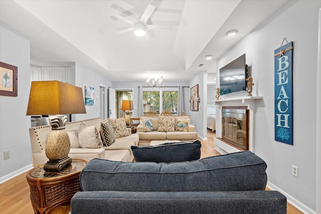 1025 Scaup Ct, Kiawah Island, SC 29455 - living room featuring a tray ceiling, light wood-style flooring, ceiling fan, a glass covered fireplace, and a chandelier