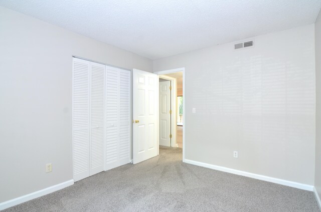 unfurnished bedroom with a textured ceiling, light colored carpet, and a closet