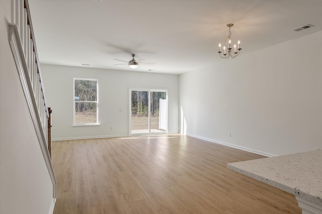 unfurnished living room featuring ceiling fan with notable chandelier, visible vents, baseboards, stairway, and light wood finished floors