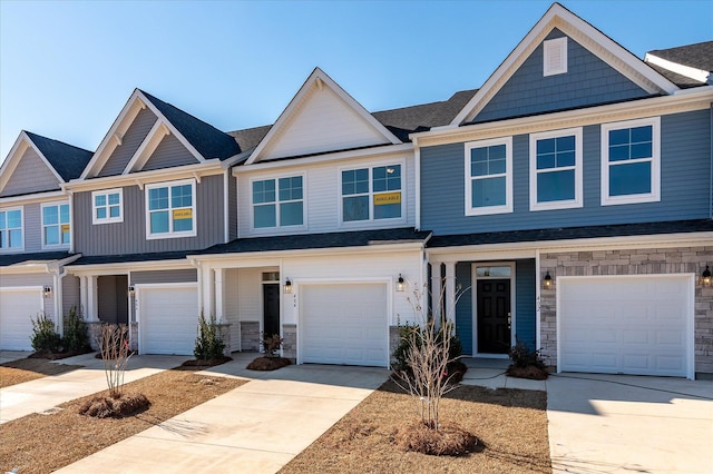 townhome / multi-family property featuring a garage, stone siding, and driveway