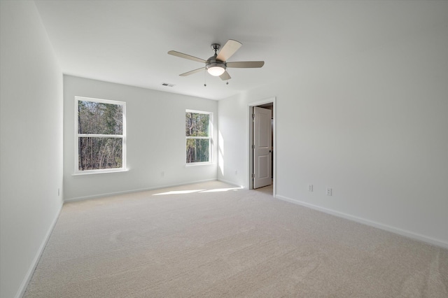 empty room featuring baseboards, visible vents, a ceiling fan, and light colored carpet