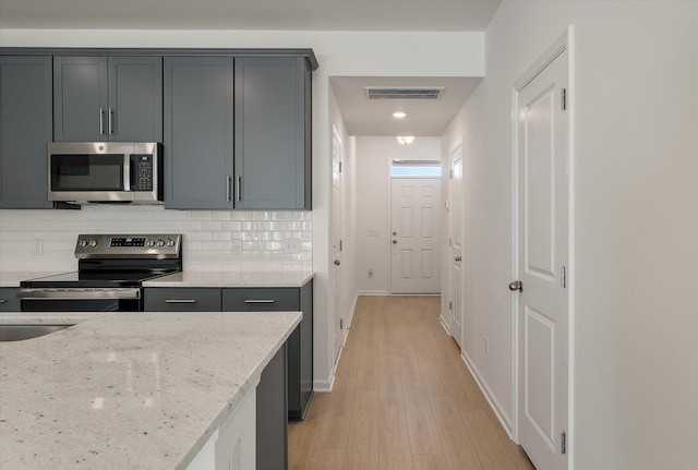 kitchen featuring light stone counters, visible vents, appliances with stainless steel finishes, light wood-type flooring, and tasteful backsplash