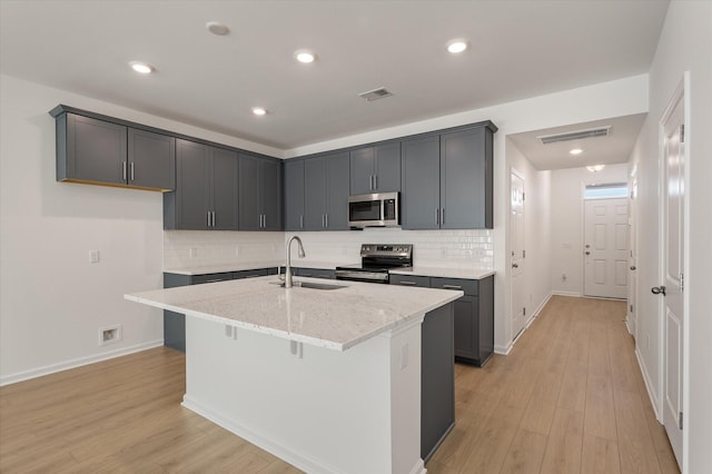 kitchen with light stone counters, a kitchen island with sink, stainless steel appliances, a sink, and gray cabinets